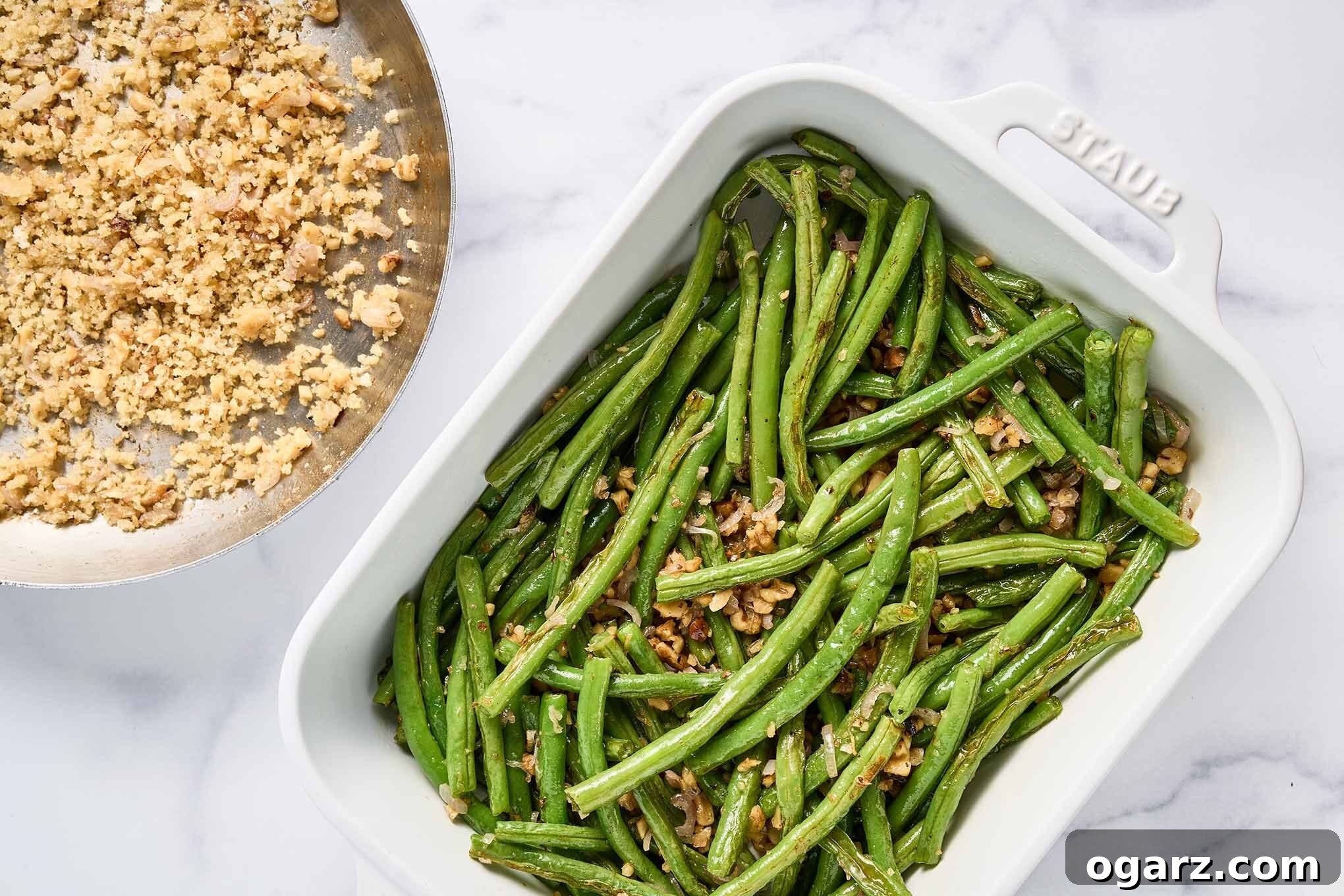 Oven-roasted green beans are carefully combined with a savory mixture of sautéed shallots and toasted walnuts in a white baking dish, ready for its final crispy topping.