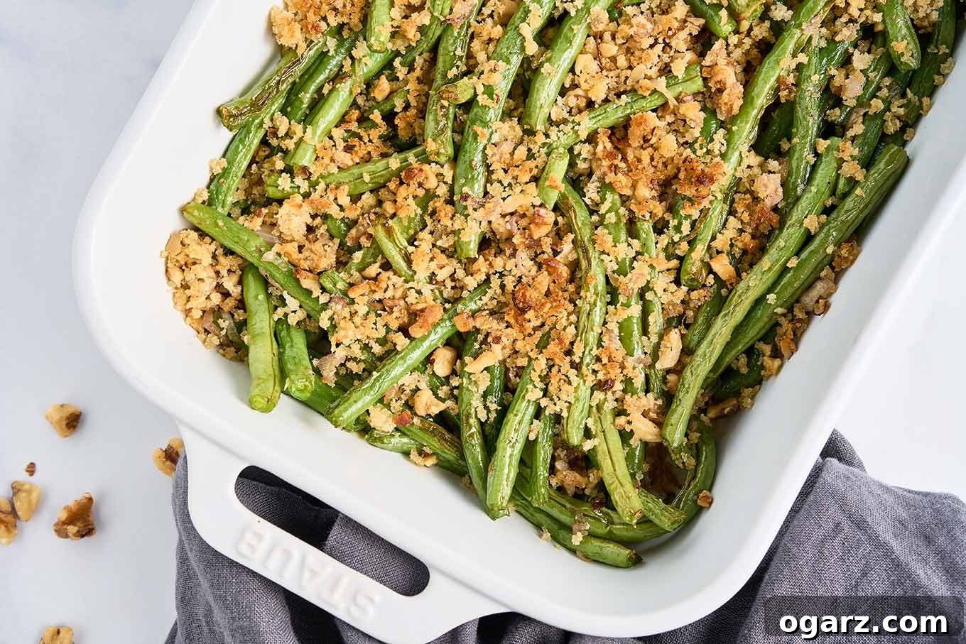 A stunning close-up of finished roasted green beans, beautifully arranged in a white casserole dish, glistening with a perfect golden-brown, crispy topping of walnuts and panko crumbs.