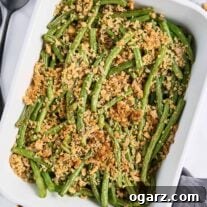 A white baking dish with fresh green beans, roasted and topped with crispy walnuts and panko crumbs.