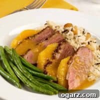 A plate with a serving of duck breast a l'orange; sliced duck breast, medium rare, orange supremes, rice pilaf, and green beans.