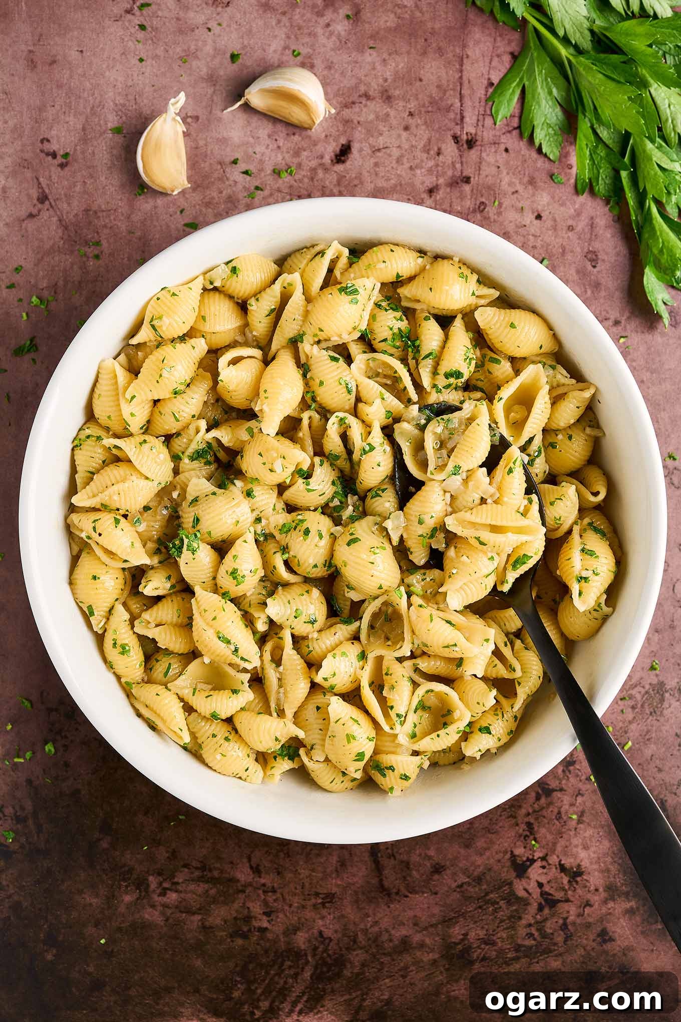 White bowl filled with cooked pasta shells tossed in garlic butter with balsamic vinegar, garnished with chopped parsley.