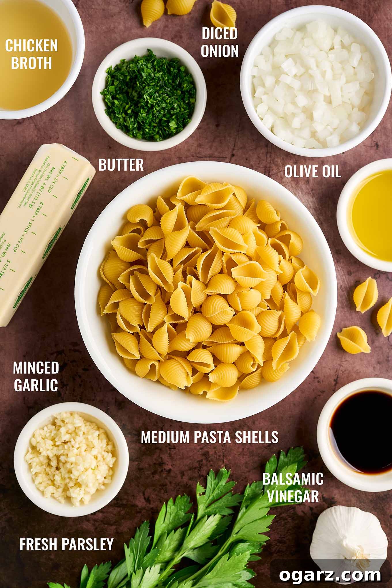 Ingredients for a garlic butter pasta side dish recipe, including pasta shells, butter, chicken broth, garlic, olive oil, onion, balsamic vinegar and parsley.