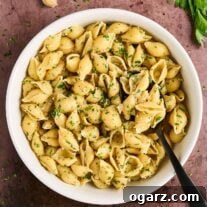White bowl filled with cooked pasta shells tossed in garlic butter with balsamic vinegar, garnished with chopped parsley.