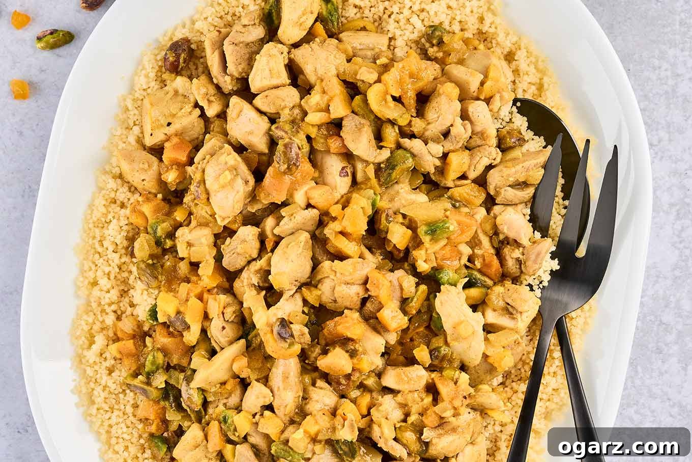 A close view of a platter of couscous topped with Persian-style apricot chicken, showing chopped pistachios, diced dried apricots, and lemon zest.