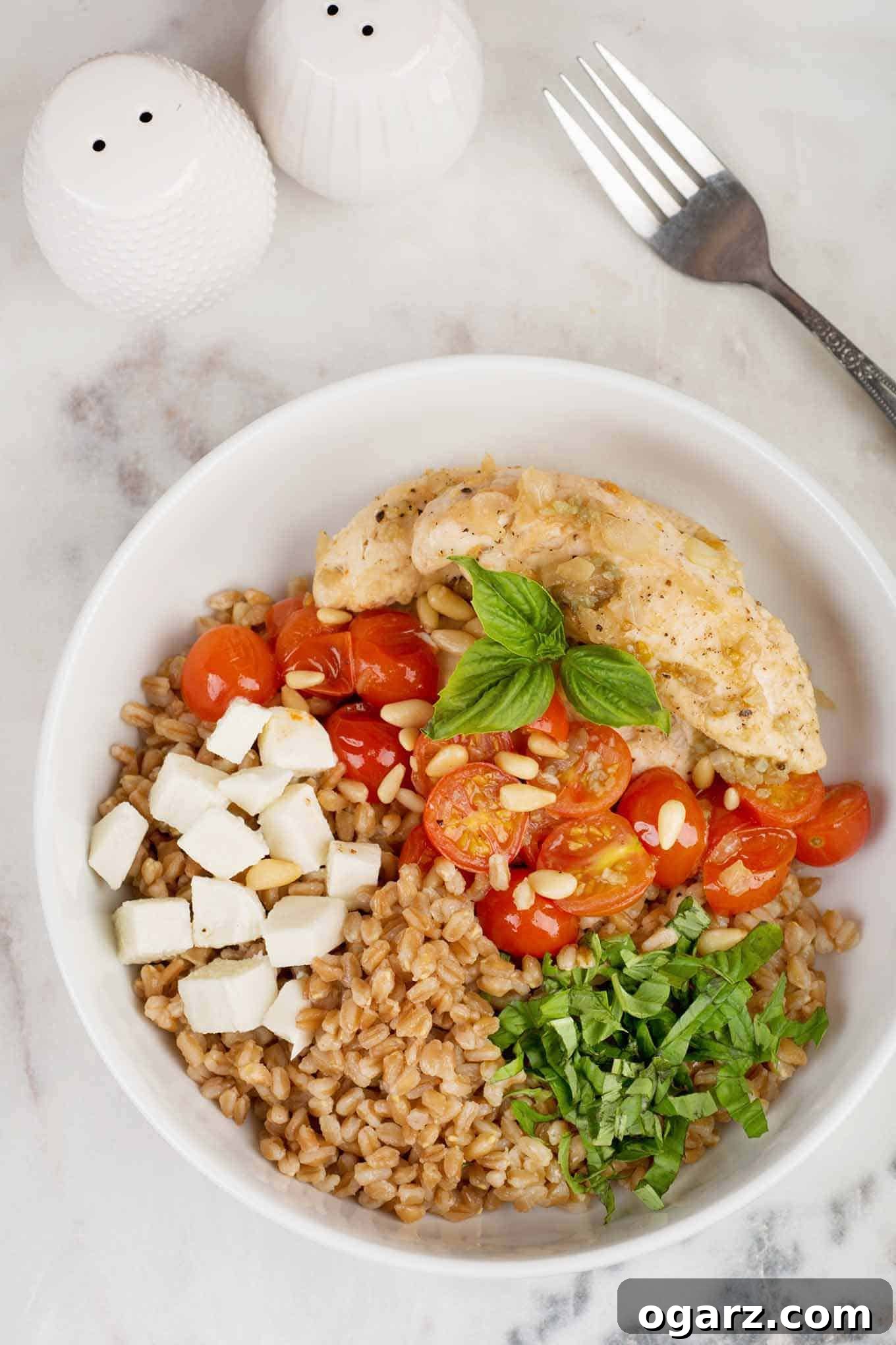 A vibrant Caprese-style farro bowl featuring perfectly pan-seared chicken, sweet sautéed grape tomatoes, fragrant fresh basil leaves, and creamy cubes of fresh mozzarella, all resting on a bed of wholesome farro.