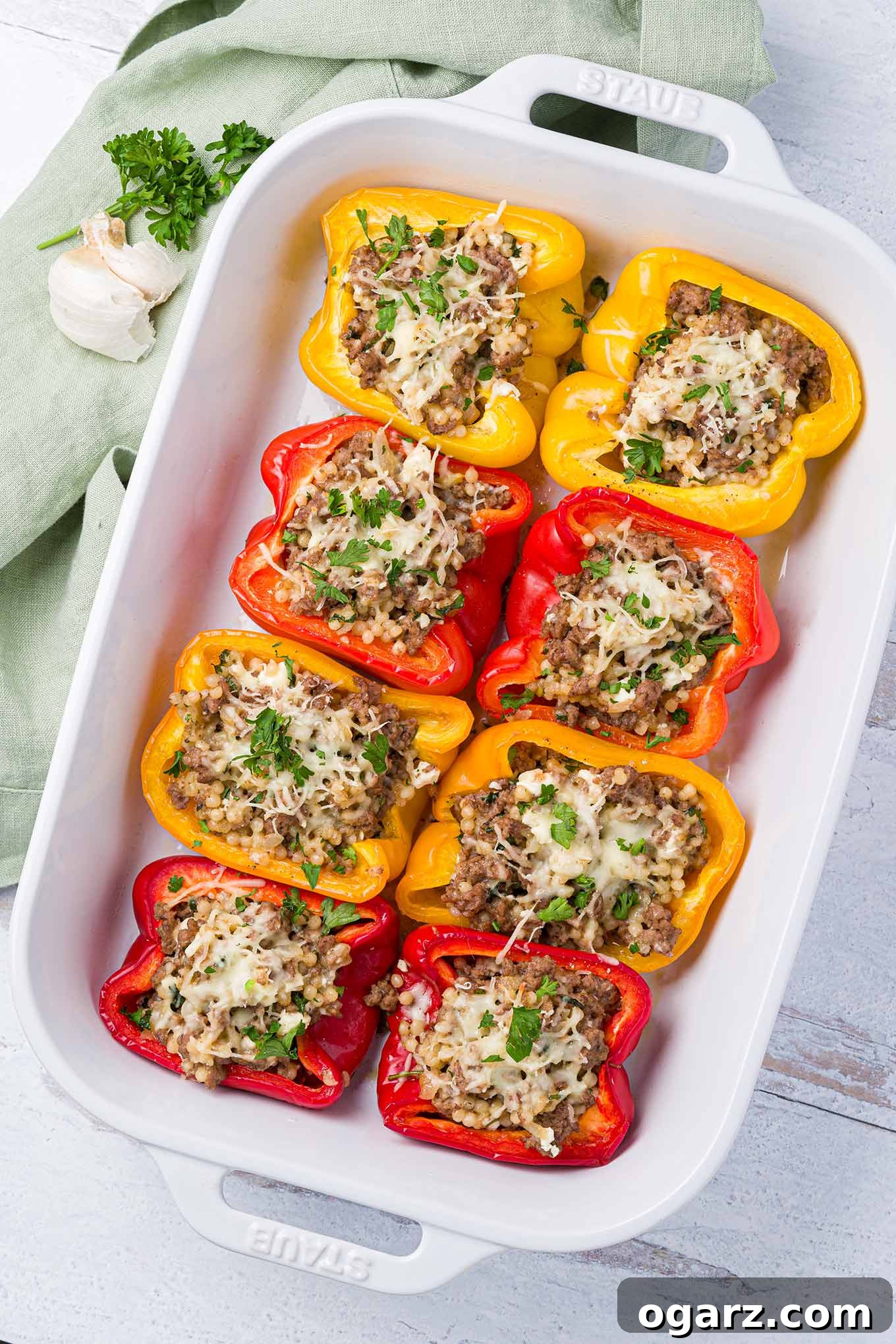 Greek Yemista 2 A white, oblong baking dish with red, yellow, and orange bell peppers stuffed with a mix of ground lamb, pearl couscous, and feta and mozzarella cheese.