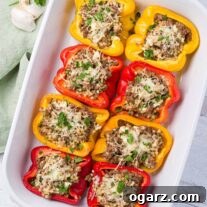 Greek Yemista 7 A white baking dish with red, yellow, and orange bell peppers stuffed with ground lamb, pearl couscous, feta, and mozzarella cheese.