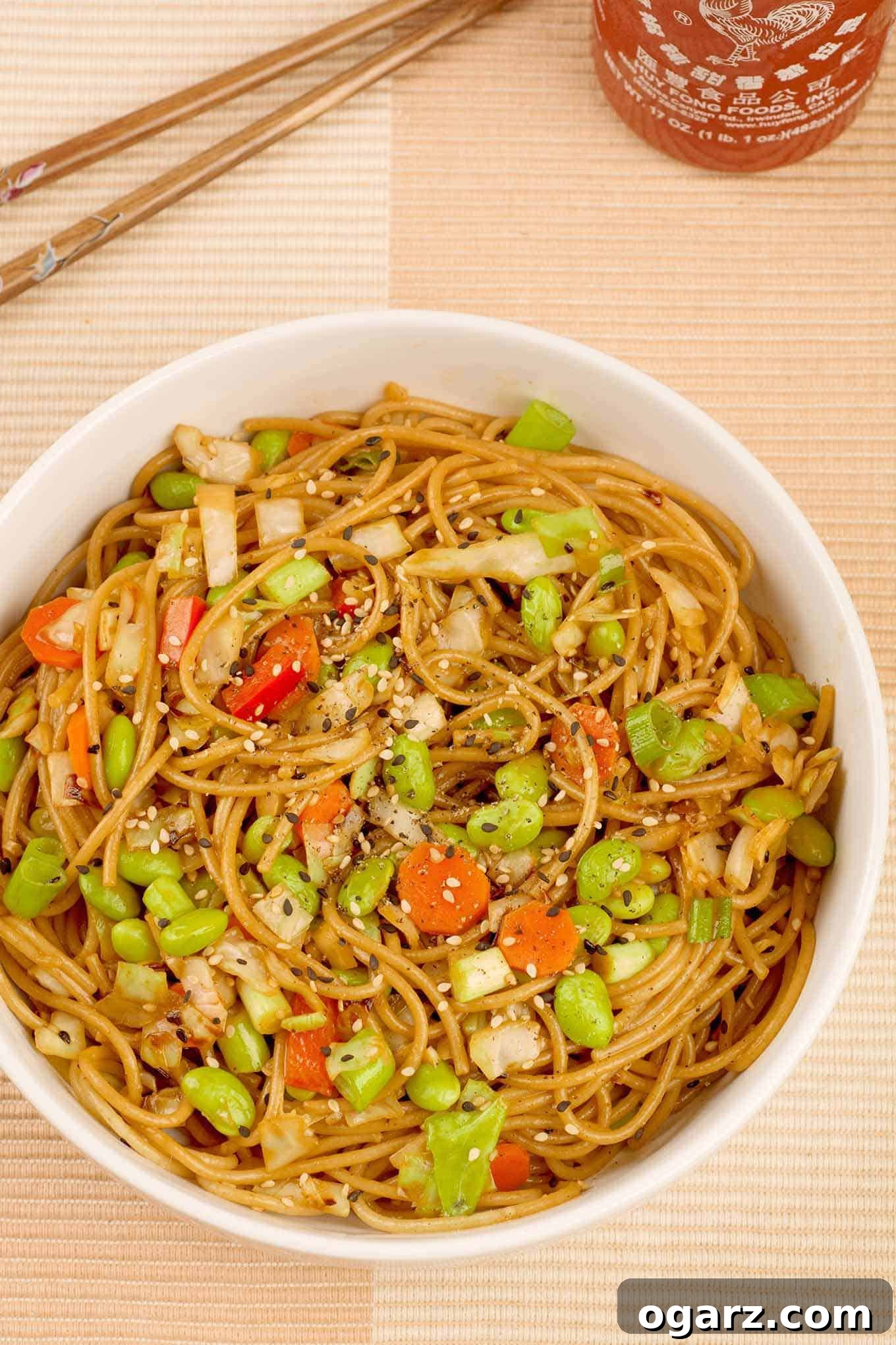 Nutty Sesame Noodles with Edamame 2 A vibrant bowl of whole wheat sesame noodles with edamame, stir-fried cabbage, carrots, red bell pepper, and scallions, all glistening with a light, creamy peanut sauce and sprinkled with sesame seeds.