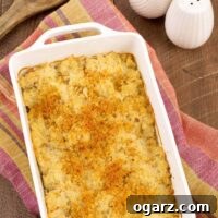 Cheesy Cauliflower Rice Gratin 4 A white, oblong casserole dish of crumb-topped, riced cauliflower gratin on a tea towel with white salt and pepper shakers in the background.