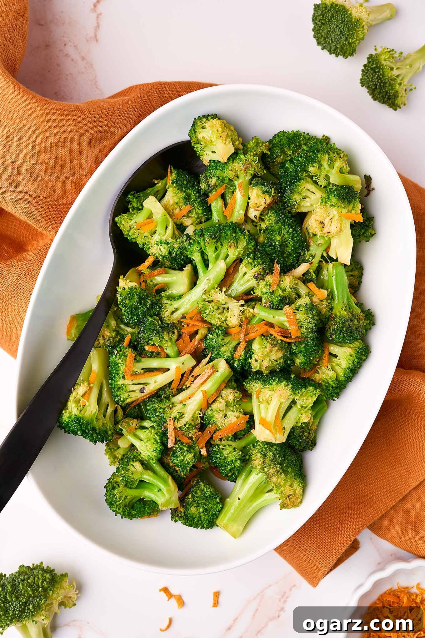 Zesty Orange Broccoli Sauté 2 A white oval serving dish of sautéed broccoli with orange peel with a black serving spoon.