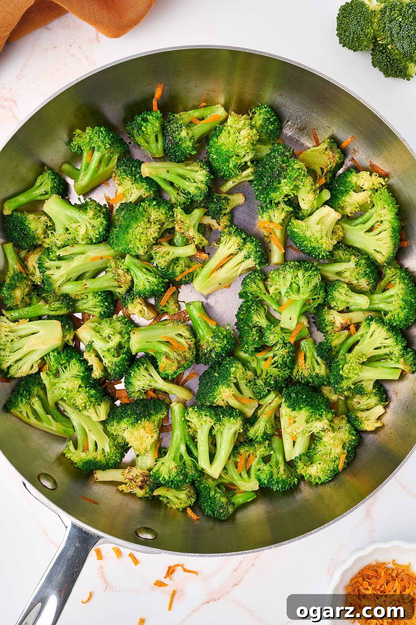 Zesty Orange Broccoli Sauté 4 Sautéing broccoli florets in a frying pan with orange peel, more orange peel in a prep bowl beside the pan.