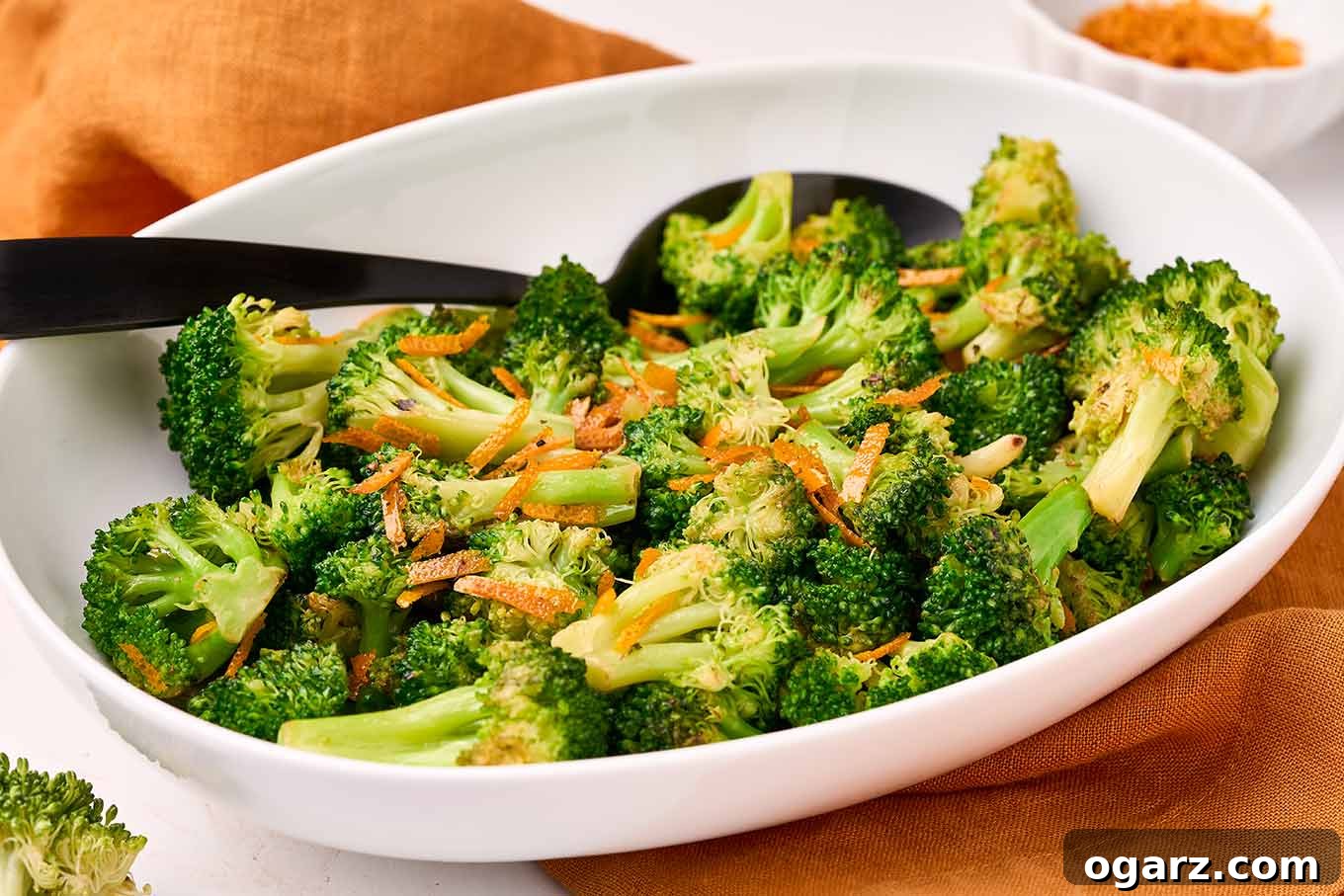 Zesty Orange Broccoli Sauté 5 A close-up of a delicious side dish featuring bright green broccoli florets seasoned with orange peel, served in a white oval dish with a black spoon.