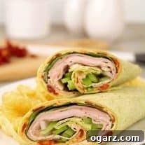 A sandwich wrap filled with sliced turkey, ham, green pepper, provolone cheese, and a sun-dried tomato spread.