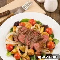A plate with a salad of grilled sirloin, baby potatoes, cherry tomatoes and mushrooms over mixed greens, napkin with fork and knife to the side.