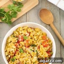 A serving bowl of pasta shells with bacon, corn, tomatoes, chipotle, cheese, and Southwest seasonings, with a cutting board, cilantro, and spoon to the side.