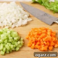 A close-up of beautifully diced mirepoix ingredients (onion, celery, and carrots) on a wooden cutting board, ready for sautéing.