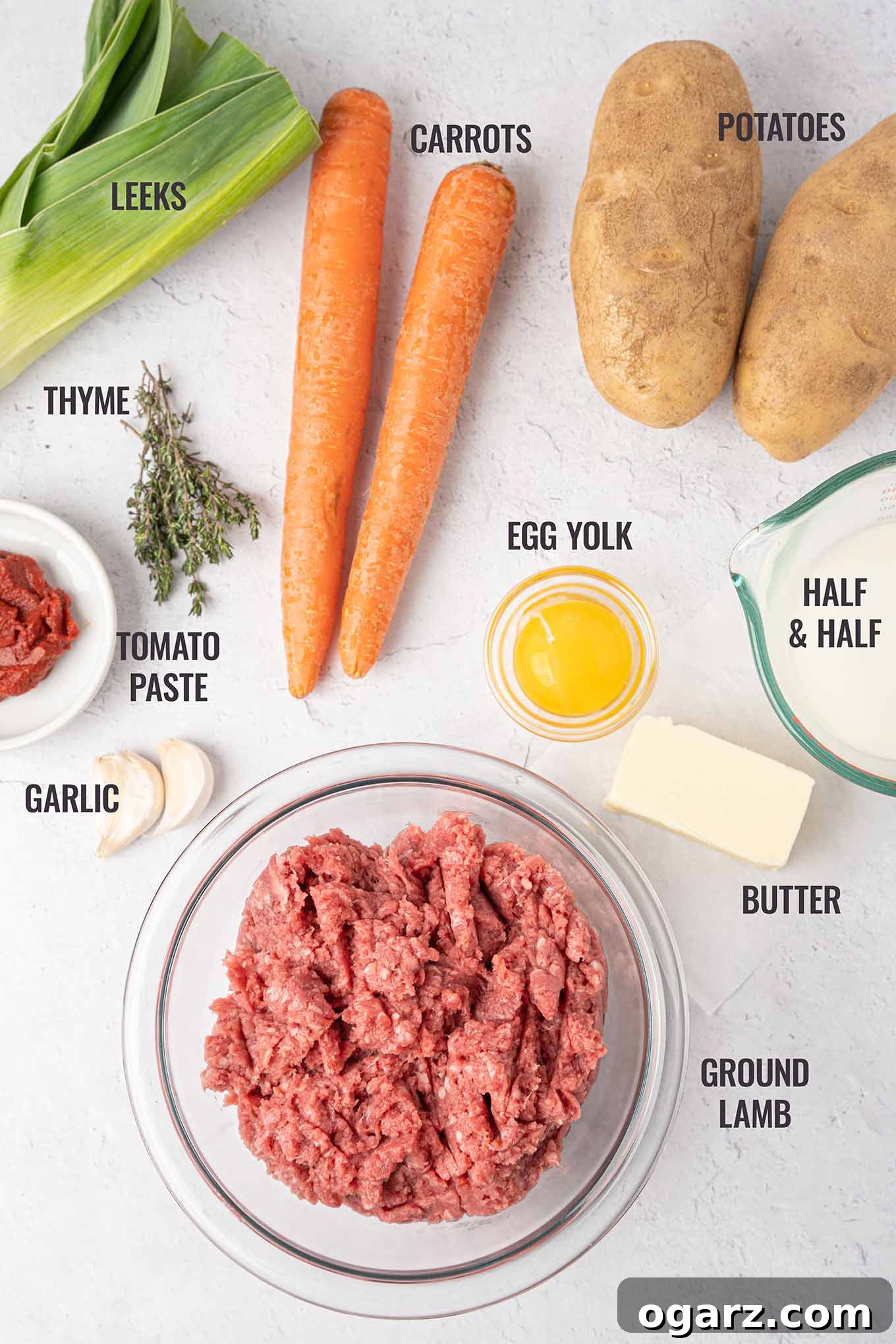 Classic Lamb Shepherd's Pie 3 A labeled photo of Shepherd\'s pie ingredients including ground lamb, garlic, egg, butter, potatoes, carrots, leeks, thyme, tomato paste, and half-and-half.