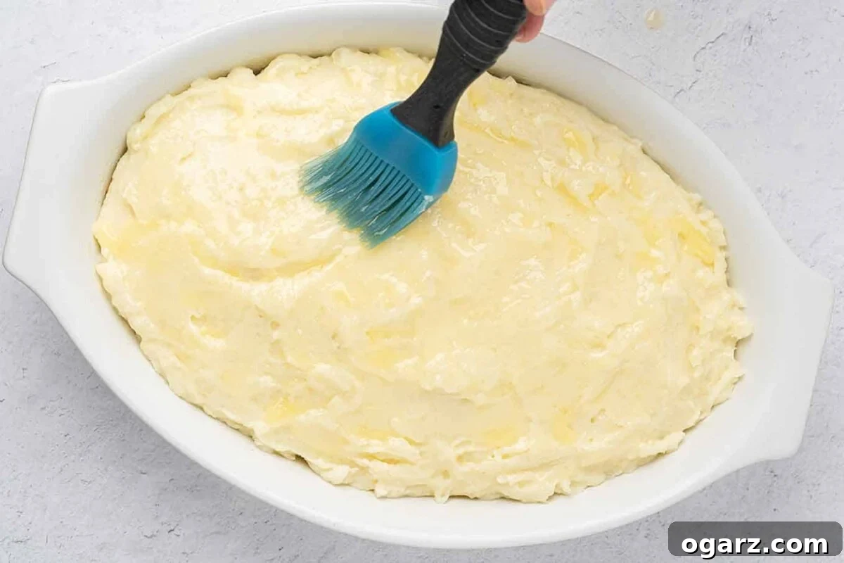 Classic Lamb Shepherd's Pie 6 White oval casserole with fully assembled shepherd's pie being brushed with melted butter before baking.
