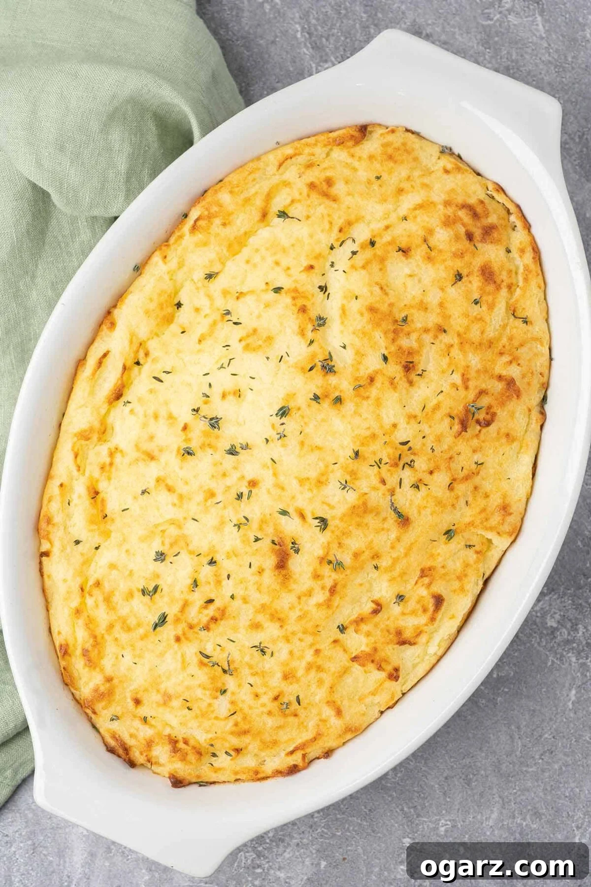 Classic Lamb Shepherd's Pie 7 Fully baked, uncut shepherd's pie in a white oval casserole with fresh thyme sprinkled on top for garnish.