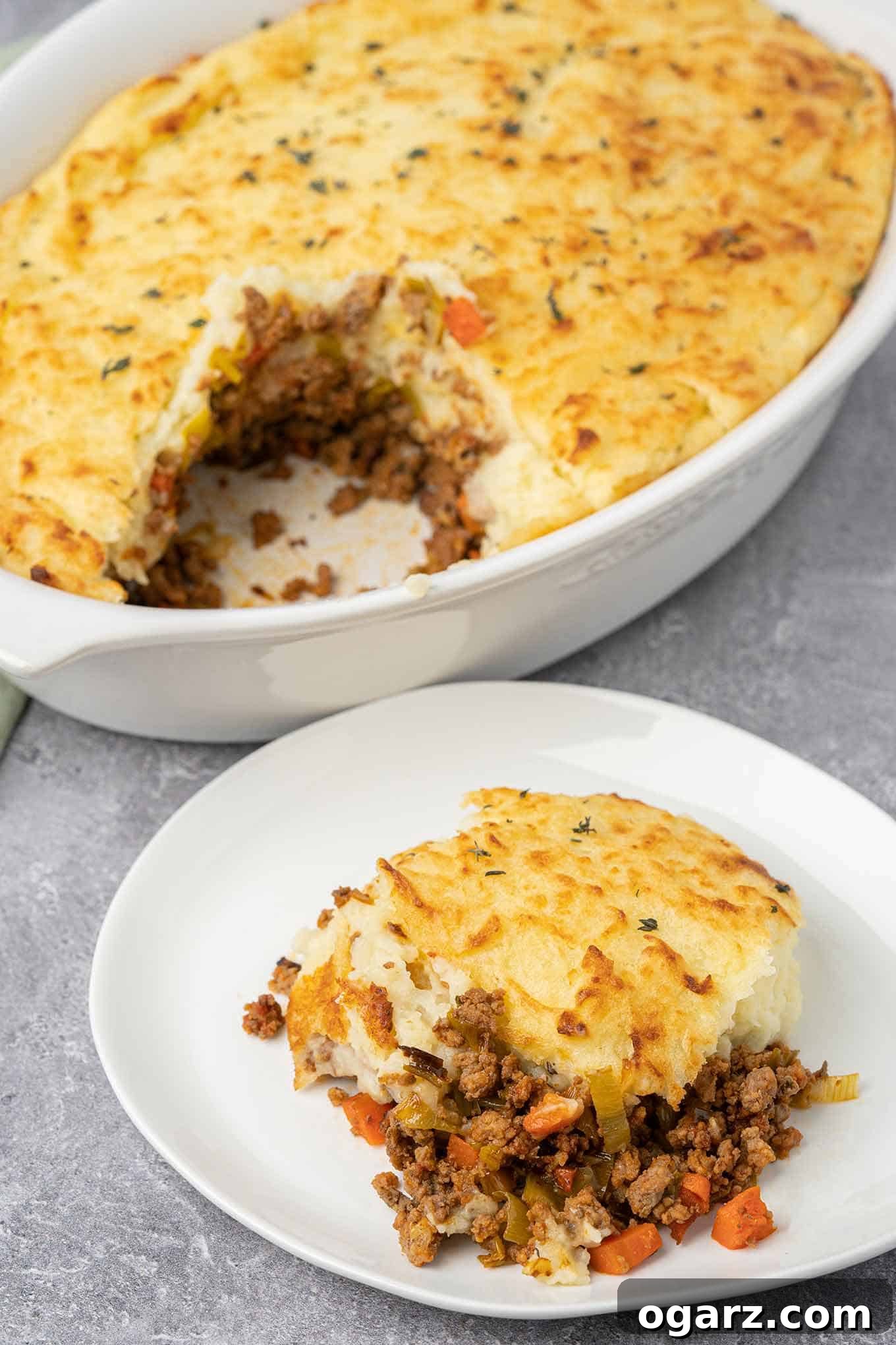Classic Lamb Shepherd's Pie 8 A serving of shepherd's pie on a plate with the partially cut casserole in the background.