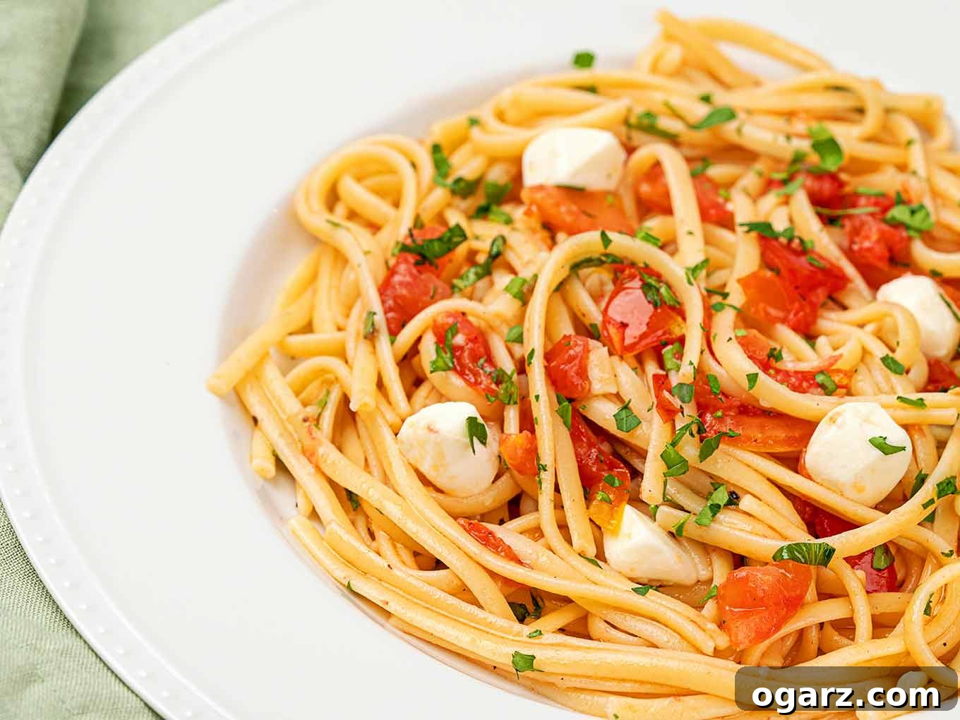 Vibrant Caprese Pasta 4 A serving of linguine tossed with chopped tomatoes, balls of fresh mozzarella, and basil in a shallow white bowl with a beaded rim.