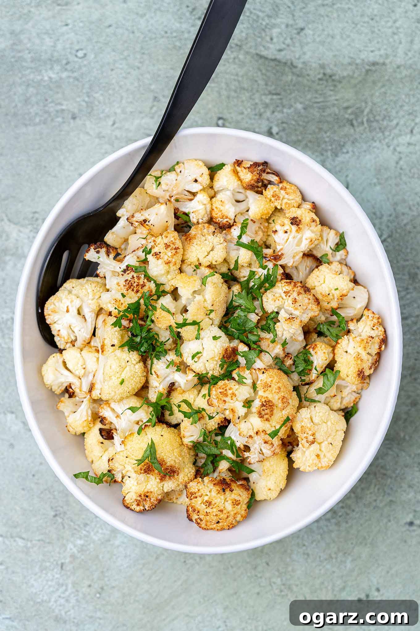 Golden Roasted Cauliflower 2 A serving bowl filled with oven-roasted cauliflower garnished with chopped parsley.