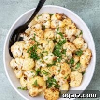 A serving bowl filled with oven-roasted cauliflower garnished with chopped parsley.