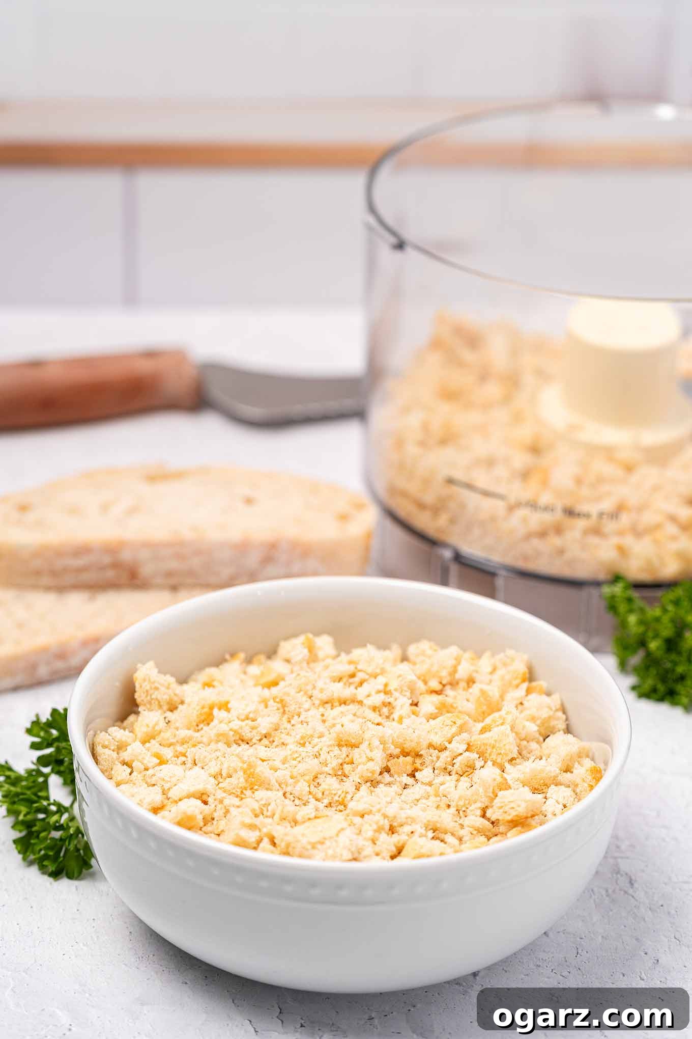 Simple Steps to Fresh Homemade Breadcrumbs 2 A crisp white bowl overflowing with freshly made breadcrumbs. In the soft background, slices of artisan bread, a sharp bread knife, and a modern food processor hint at the preparation process.