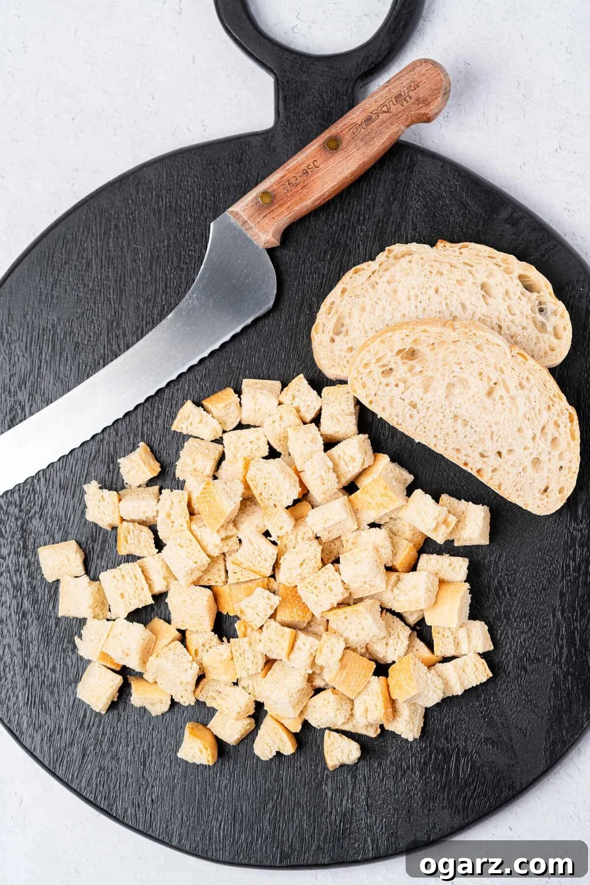 Simple Steps to Fresh Homemade Breadcrumbs 3 A dark wooden cutting board holds neatly cut cubes of bread, demonstrating the ideal size for processing into fresh breadcrumbs. Adjacent, whole slices of bread and a bread knife await preparation.