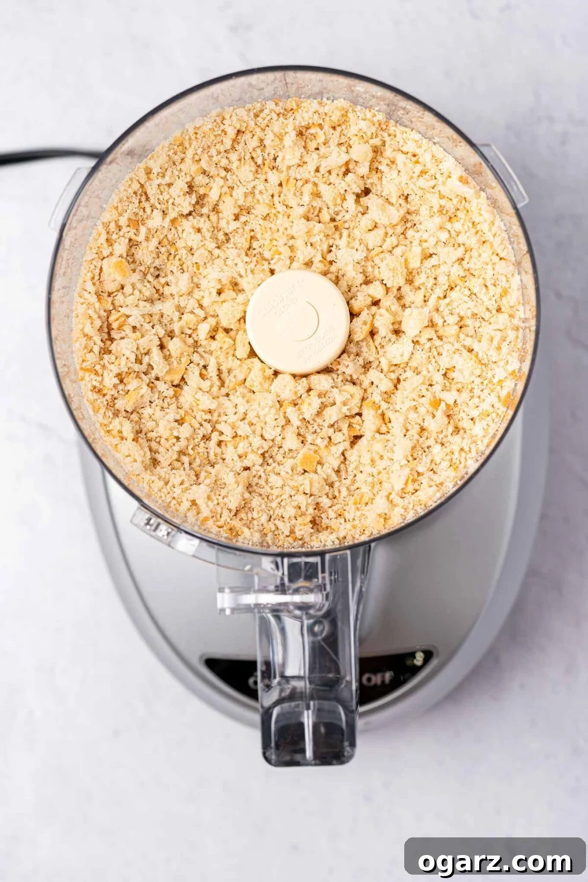 Simple Steps to Fresh Homemade Breadcrumbs 4 An overhead view captures fresh, coarse breadcrumbs inside the work bowl of a food processor, showcasing their medium size and slightly irregular texture after being processed.