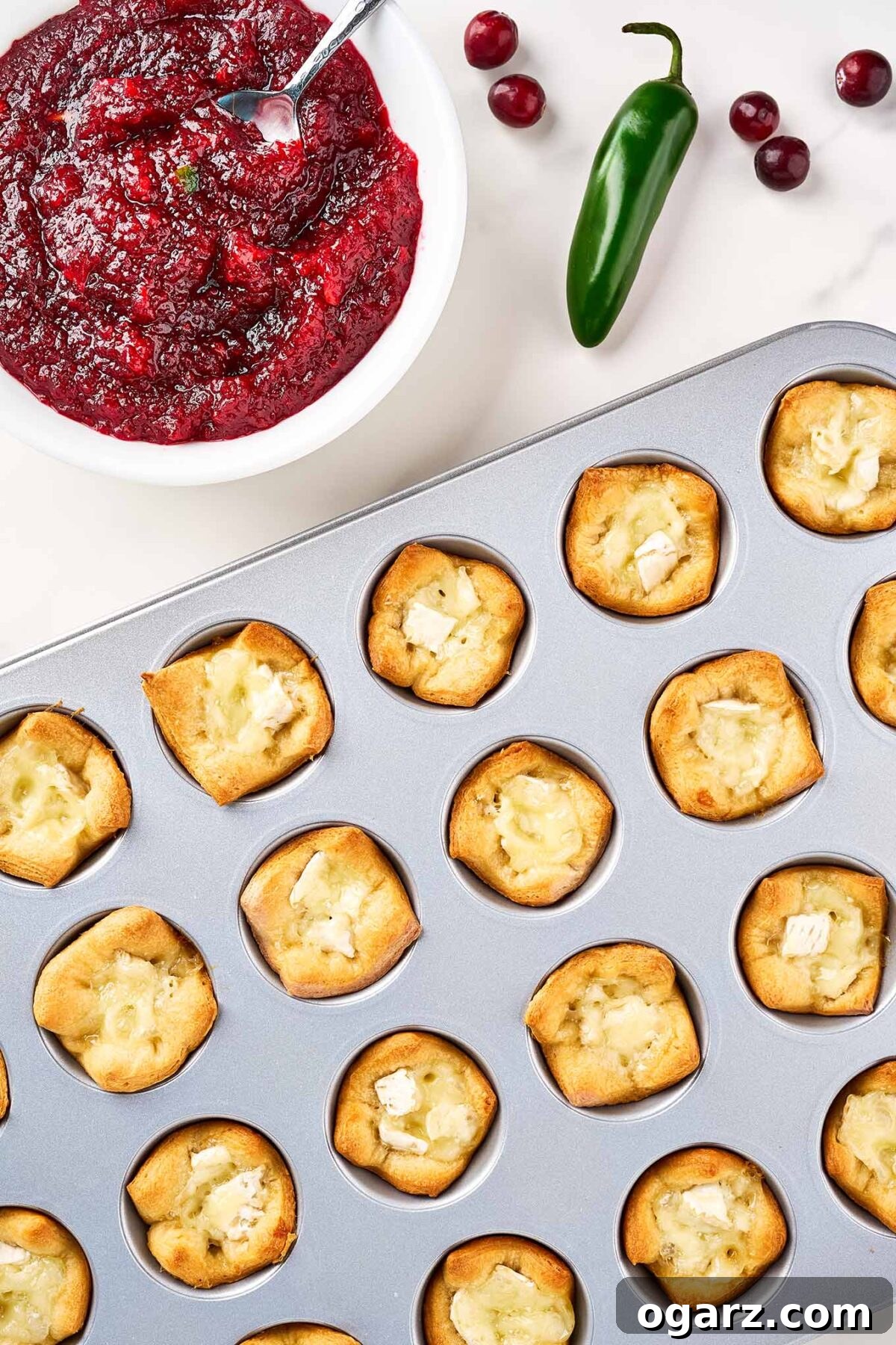 A mini muffin tin filled with baked brie bites ready to be topped with the homemade cranberry jam.