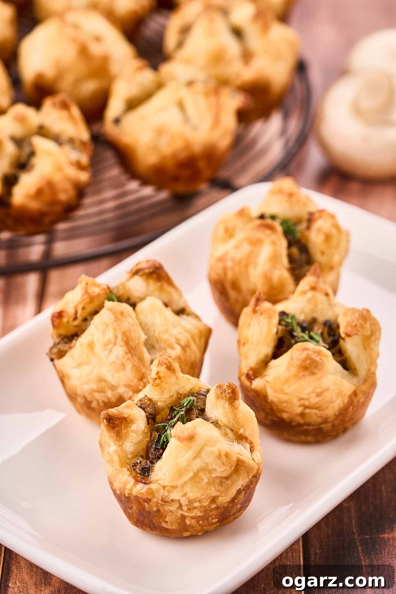 Umami Mushroom Puffs 4 A close-up of mushroom puffs garnished with fresh thyme on an appetizer plate, more in the background.