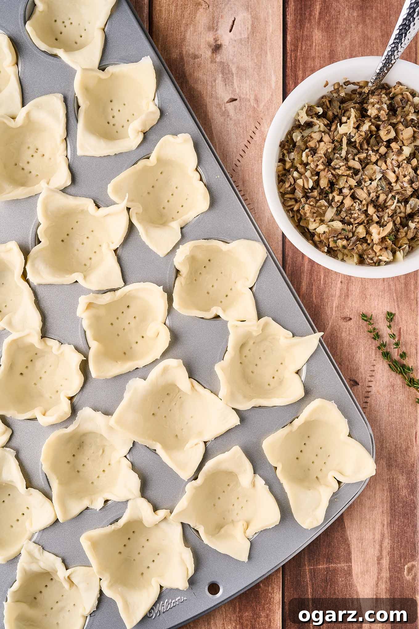 Umami Mushroom Puffs 6 A mini muffin tin filled with squares of puff pastry, perforated on the bottom and ready to be filled with the sautéed mushroom mixture in a bowl on the right.