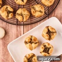 An overhead view of mushroom puff pastry appetizers on a cooling rack next to a small serving plate with four mushroom puffs on it.