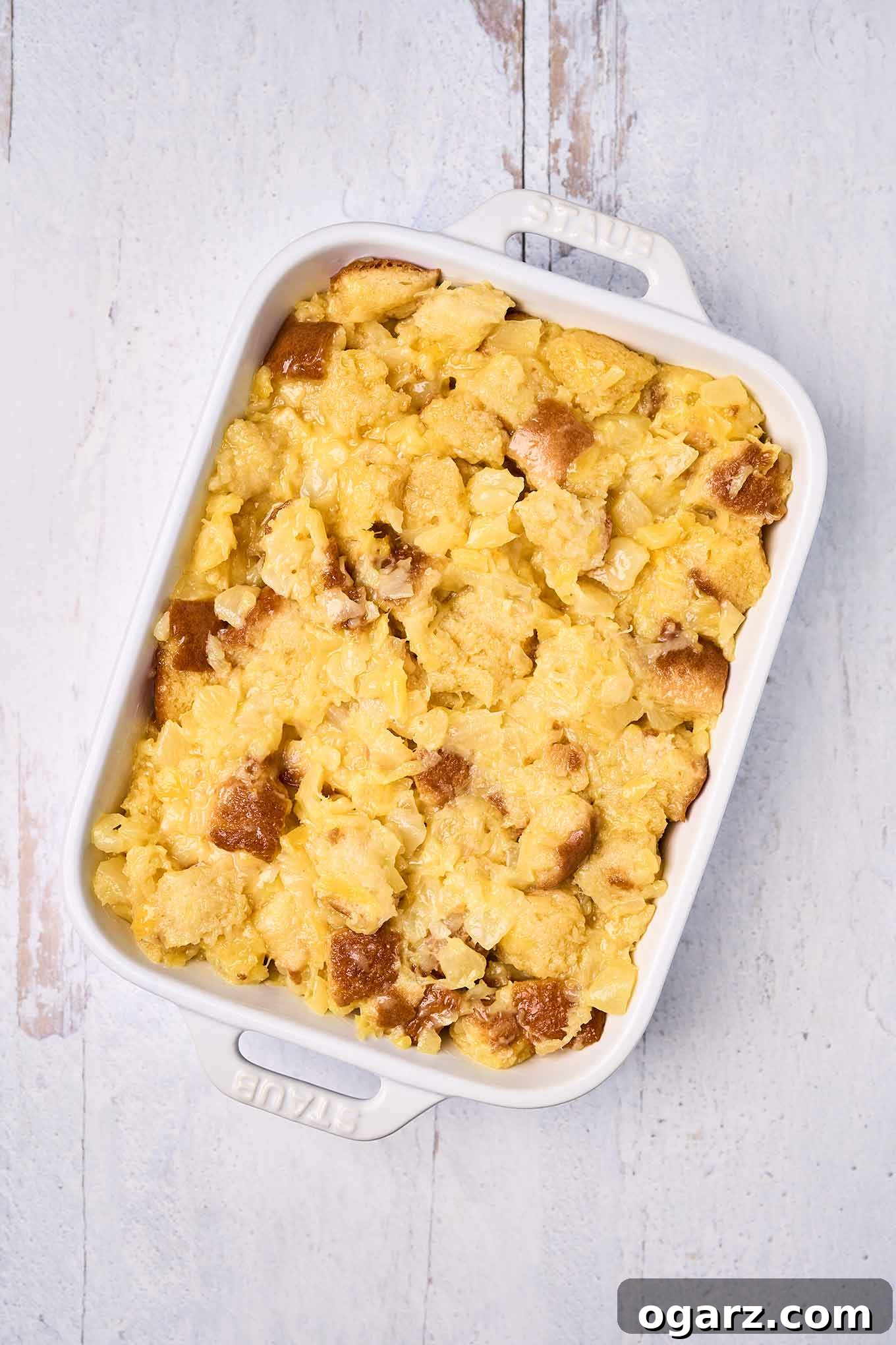 Golden Pineapple Gratin 5 The combined ingredients for scalloped pineapple – brioche bread, crushed pineapple, eggs, and melted butter – expertly spread within a casserole dish, poised and ready for baking to golden perfection.
