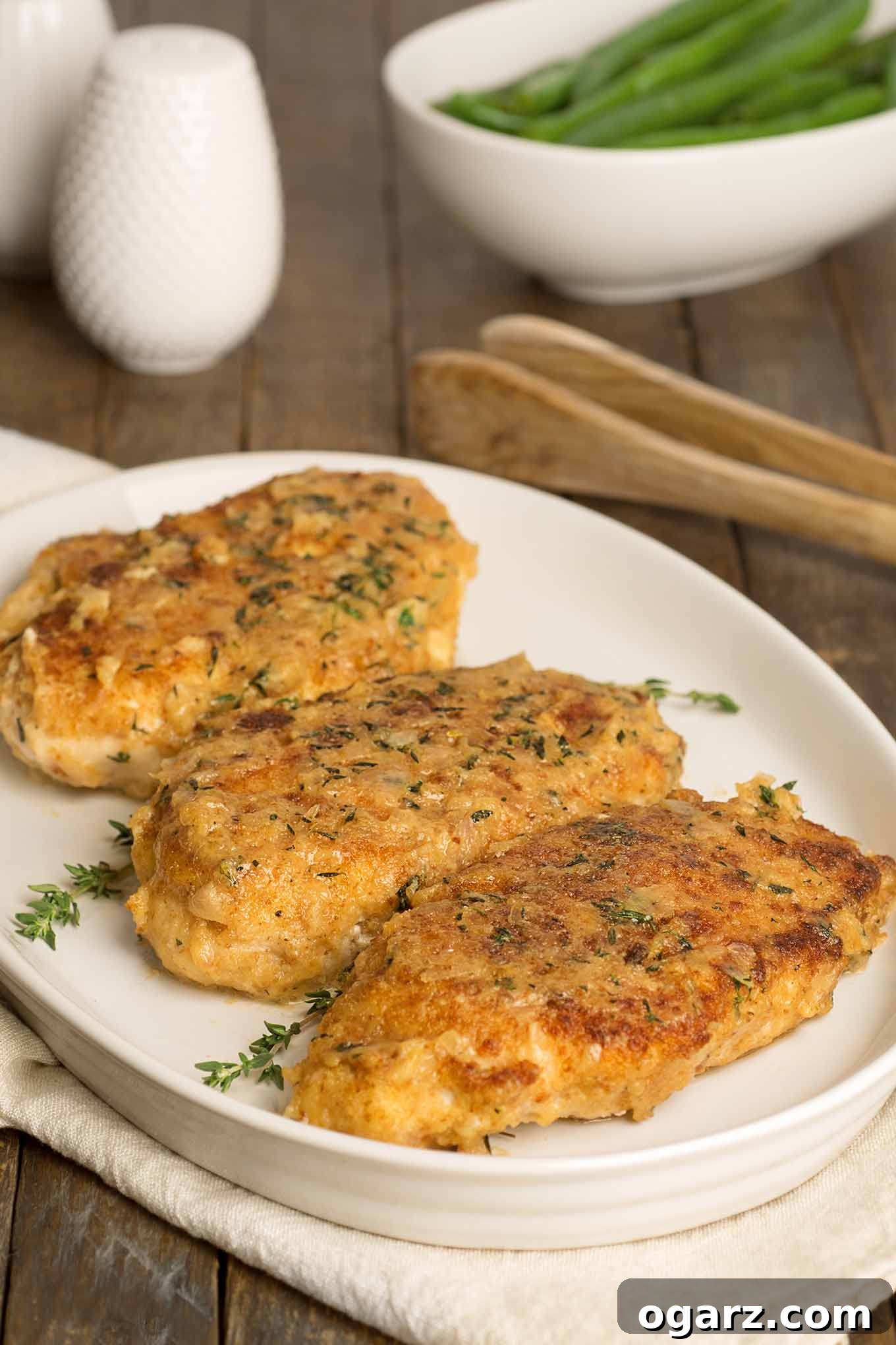 Golden Crispy Chicken Cutlets 2 Crispy, golden breaded chicken cutlets topped with a light shallot and thyme glaze, served on a white platter with fresh green beans in the background.