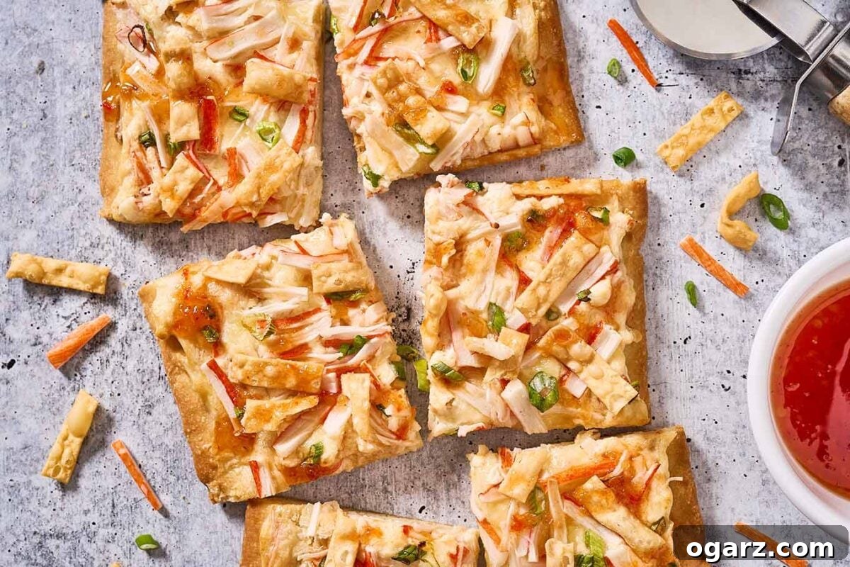 Crab Wonton Pizza 8 Squares of crab Rangoon flatbread on a gray surface surrounded by a pizza cutter, dipping bowl of sweet Thai chili sauce, and bits of ingredients.