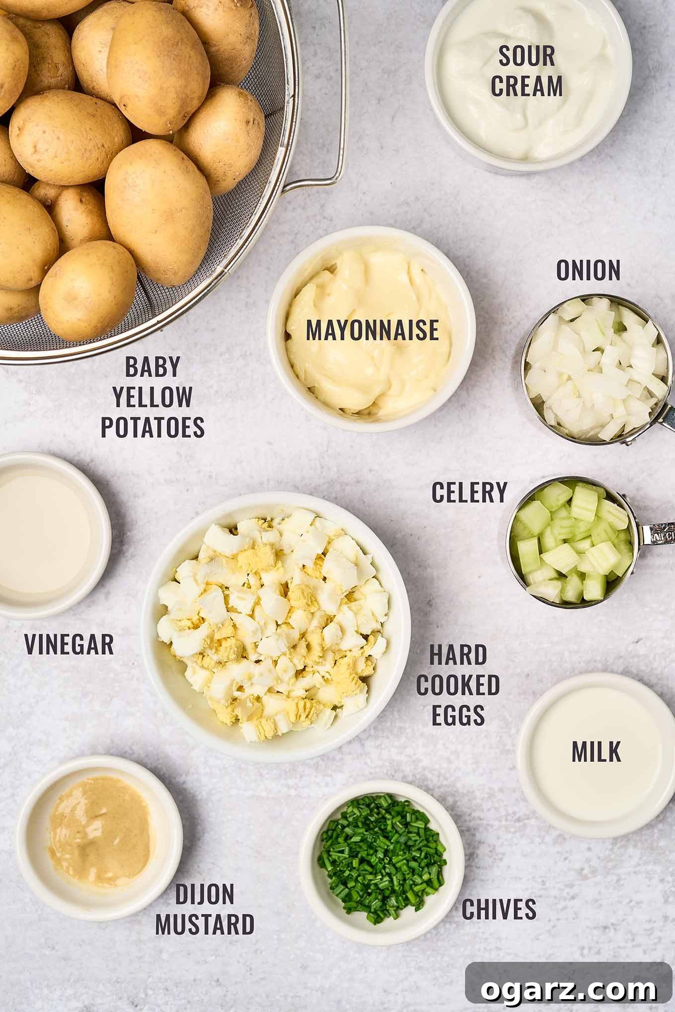 Sour Cream Potato Salad: A Zesty Twist on a Classic Side 3 A labeled, overhead view of the ingredients for sour cream potato salad; baby yellow potatoes, sour cream, mayonnaise, onion, celery, hard boiled eggs, milk, chives, Dijon mustard, and vinegar.