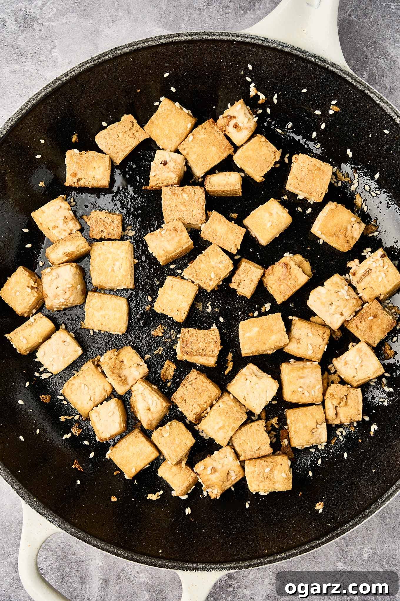 Golden brown cubes of perfectly sautéed, extra-firm tofu glistening with sesame seeds in a rustic cast iron pan, ready to be added to the Asian noodle salad.