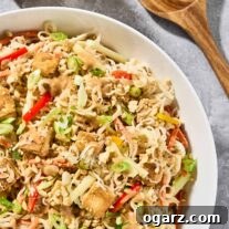 A serving bowl of Asian noodle salad with peanut dressing and crispy, golden tofu, extra peanut dressing and salad servers to the side.