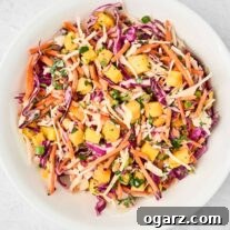 A white bowl of pineapple slaw made with red and green cabbage, shredded carrots, chunks of fresh pineapple, scallions, cilantro, and a tangy dressing.