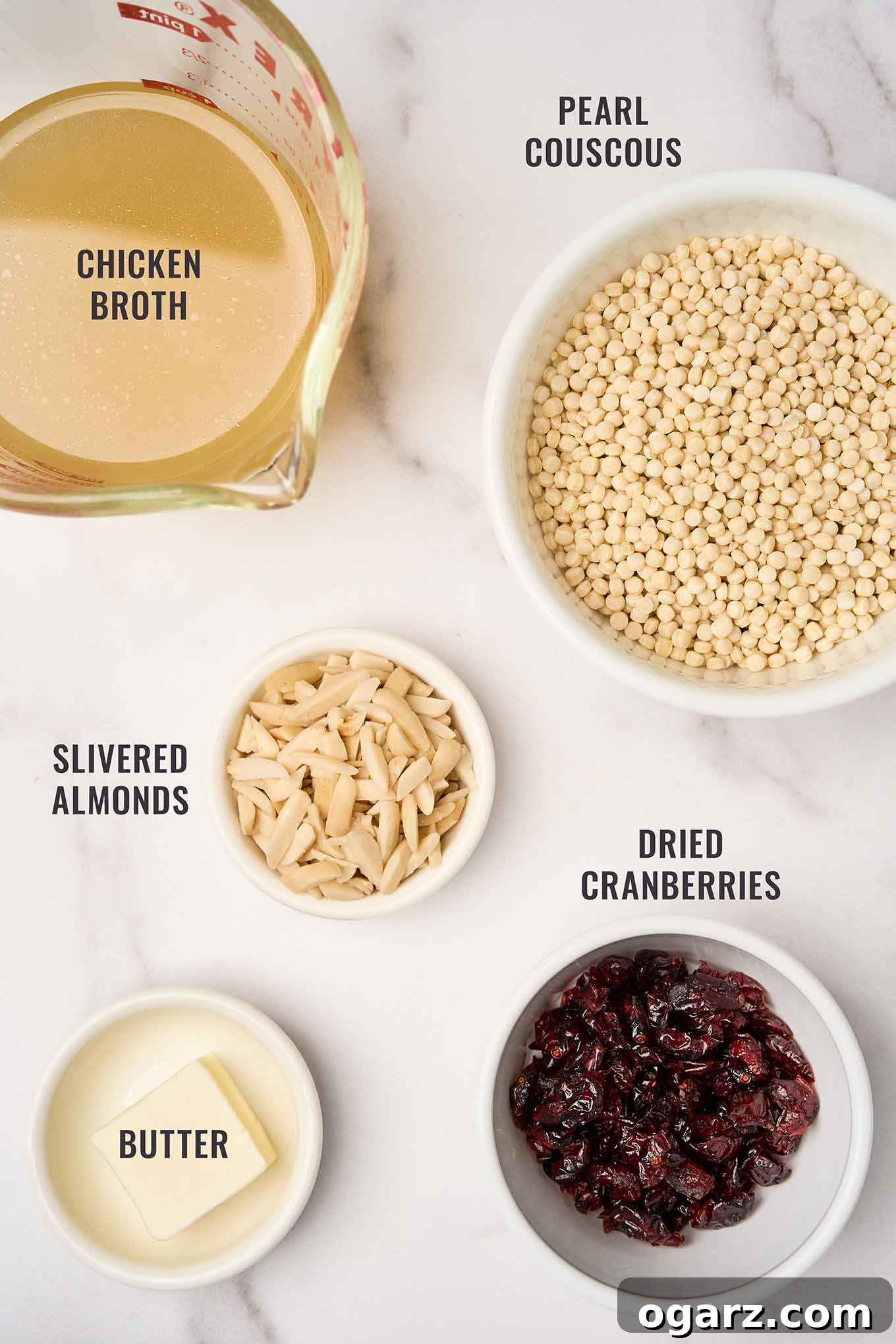 A labeled, overhead photo of the ingredients needed to make pearl couscous with cranberries and almonds; pearl couscous, chicken broth, butter, slivered almonds, and dried cranberries.