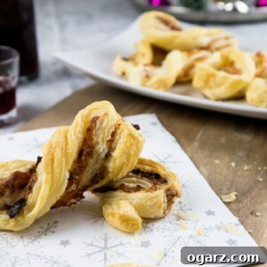 A festive napkin with a bacon and cheese puff pastry twists on a wooden cutting board. There's a white, rectangular plate in the background with more of the puff pastry twists.
