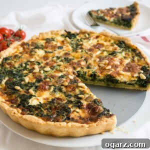 A spinach quiche with cheese and pine nuts on a springform bottom with a slice missing. There's a white plate with a slice in the background.