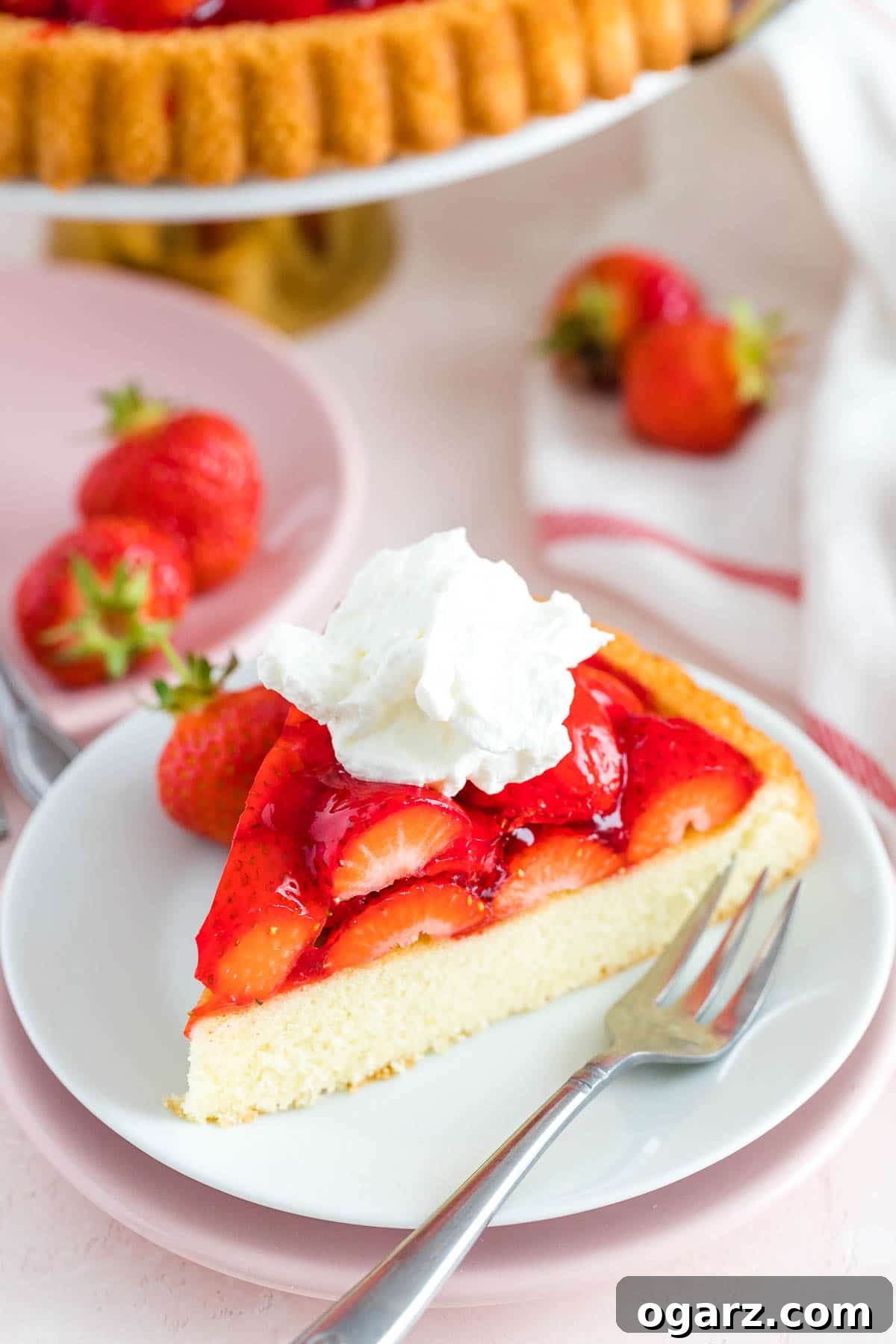 German Strawberry Kuchen 2 A perfectly sliced German Strawberry Cake on a white plate, revealing layers of soft cake, fresh strawberries, and a glossy red glaze. A fork rests beside it, inviting a taste.