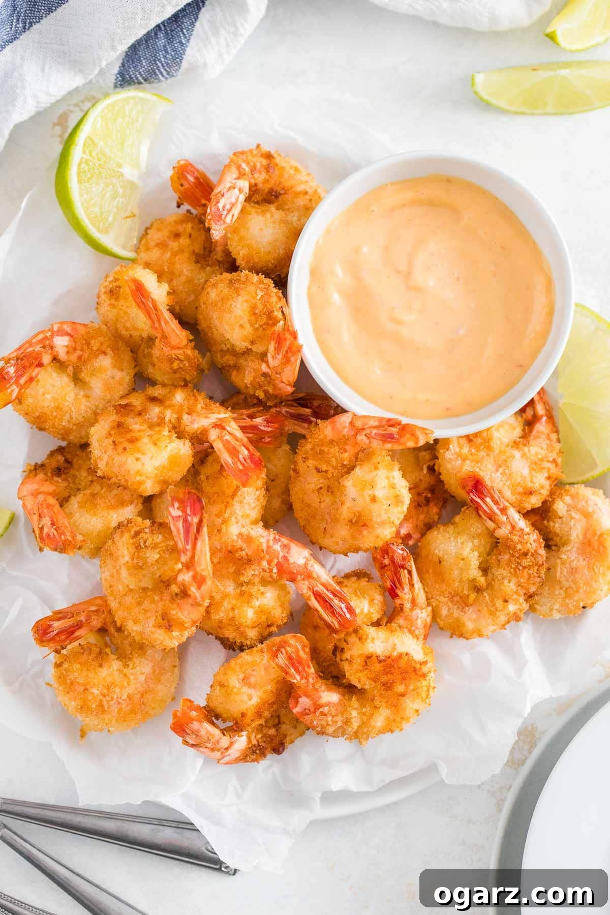 Crispy Golden Air Fryer Coconut Shrimp 2 Crispy, golden Air Fryer Coconut Shrimp on white parchment paper, ready to be served with a small bowl of dipping sauce.