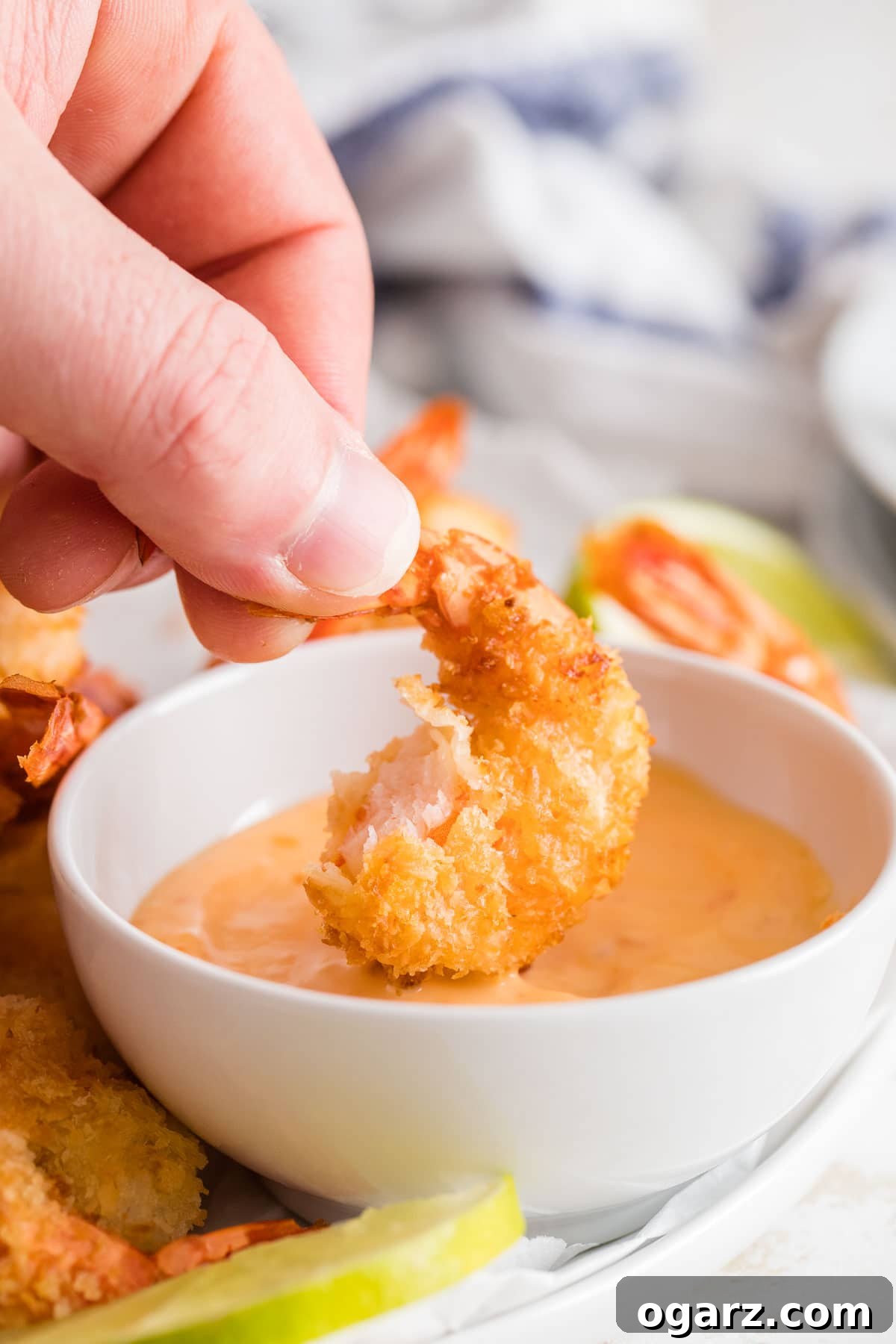 Crispy Golden Air Fryer Coconut Shrimp 7 A single air-fried coconut shrimp being dipped into a vibrant orange sauce, highlighting its crispy texture.