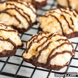 Irresistible coconut macaroons with decadent chocolate-dipped bottoms and elegant chocolate stripes, cooling on a sleek black rack.
