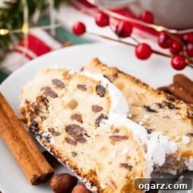 Two generous slices of classic Christstollen, elegantly presented on a white plate and garnished with fragrant cinnamon sticks, vibrant cranberries, and whole hazelnuts.