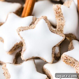 A close-up view of delicate Zimtsterne (Cinnamon Stars), elegantly garnished with a cinnamon stick, showcasing their intricate star shape and snowy white icing.